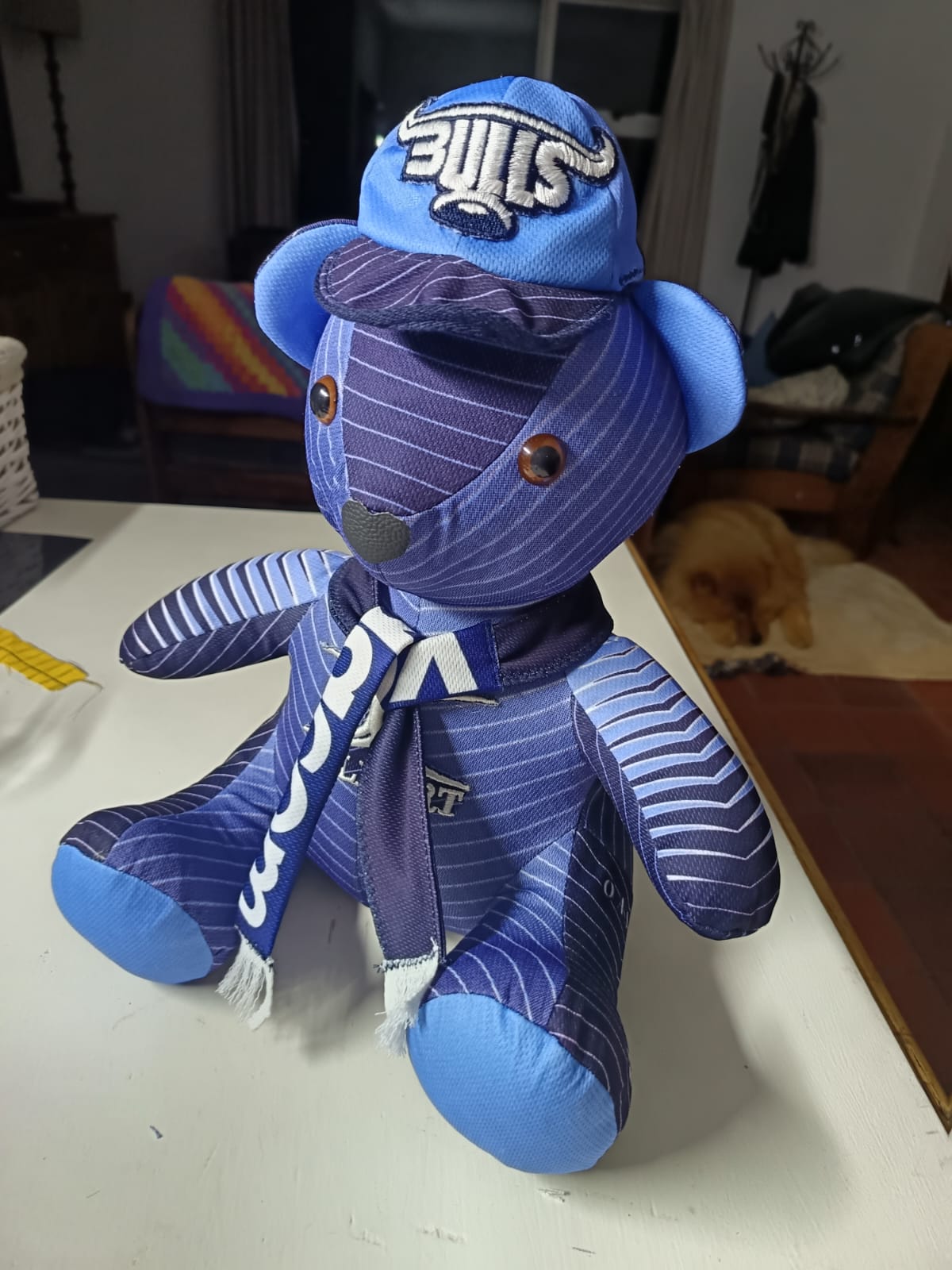 A navy teddy bear sewn from a pinstriped Bulls rugby jersey, with light blue ears and foot pads, a cap with the embroidered Bulls logo and a team scarf